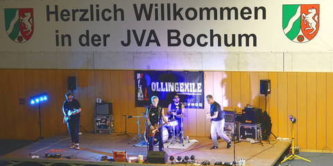 Die vierköpfige Band auf der Bühne in der Mehrzweckhalle unter dem Banner der JVA.